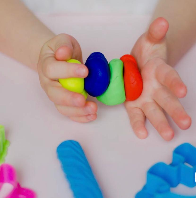 Mains d&rsquo;enfant façonnant des boules de pâte à modeler colorées.
